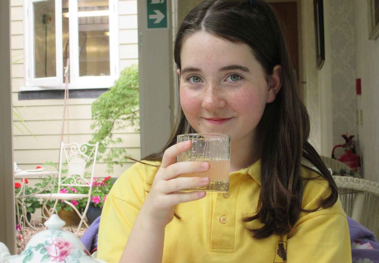 Kira holding a drink and wearing a yellow top