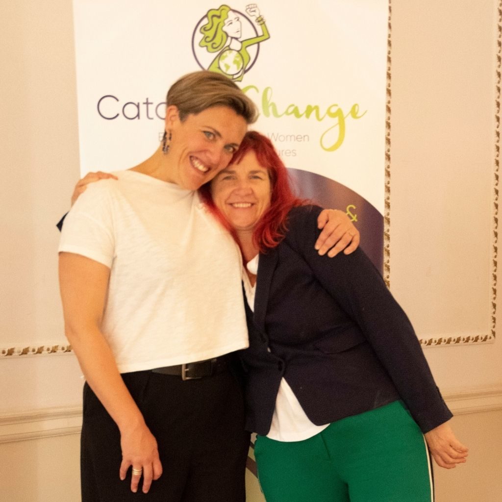 Traci and Jenna posing for a photo in front of the Catalyse Change logo