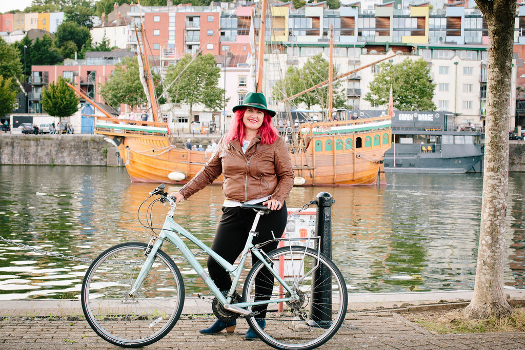 Traci standing in front of Bristol Harbour with her bike