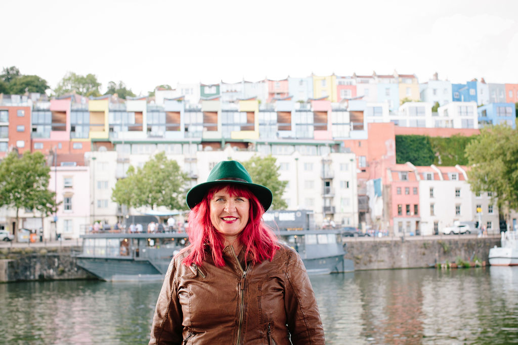 Traci standing in front of Bristol Harbour wearing a hat
